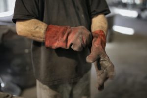 Trade worker wearing work gloves that are worn in, t-shirt and jeans